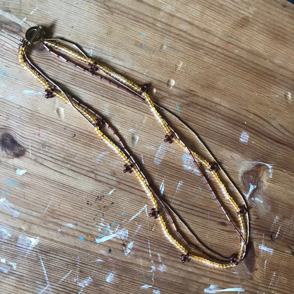 THREE STRAND GOLD COLOUR BEAD NECKLACE LAYING ON WOOD TABLE
