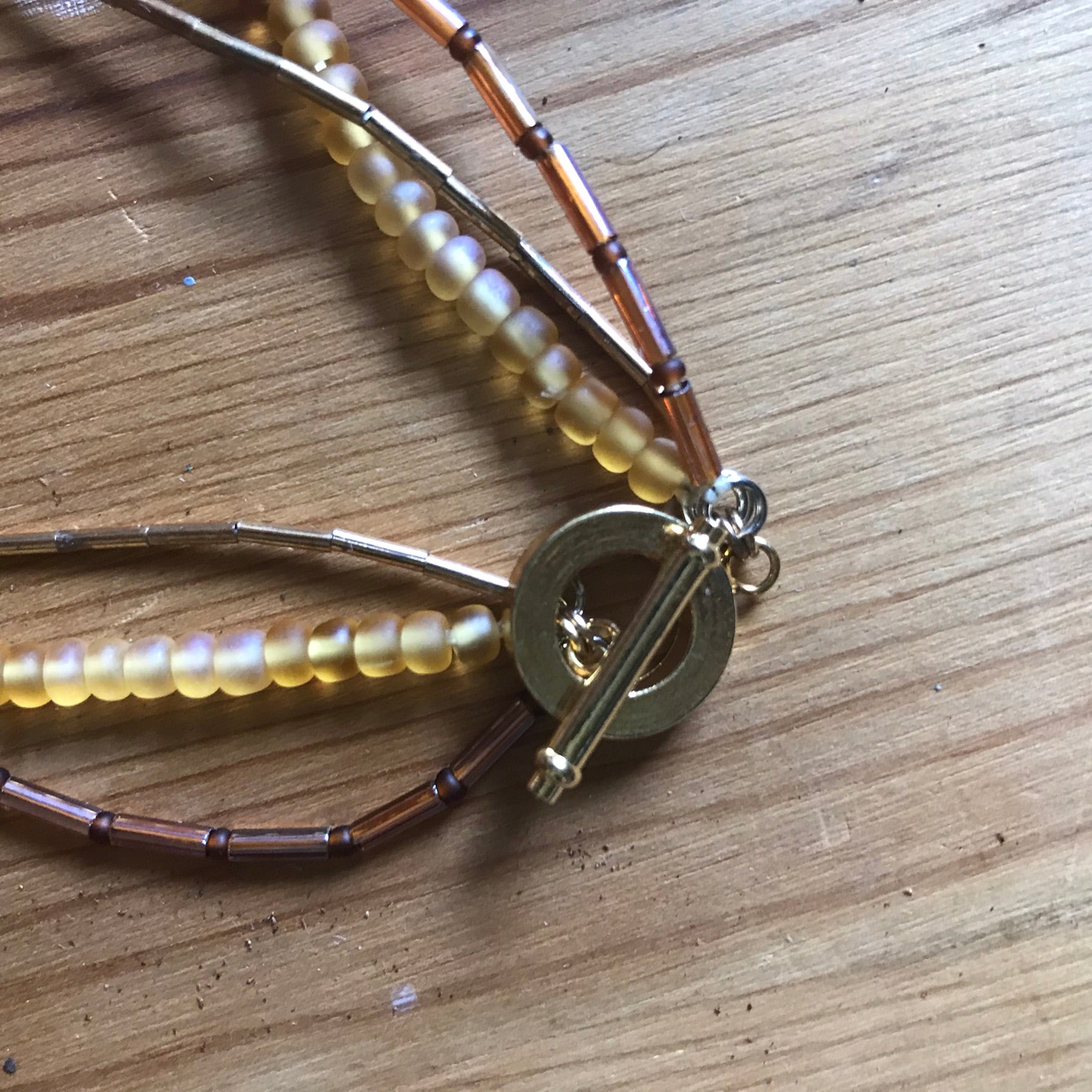 CLOSE UP OF THREE STRAND GOLD COLOUR BEAD NECKLACE TOGGLE CLASP