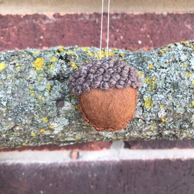 ACORN EMBROIDERED ORNAMENT DISPLAYED IN FRONT OF LICHEN COVERED BARK